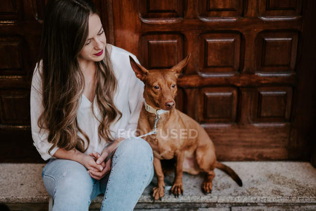 Casual woman with hound dog sitting on concrete step on street — Stock Photo