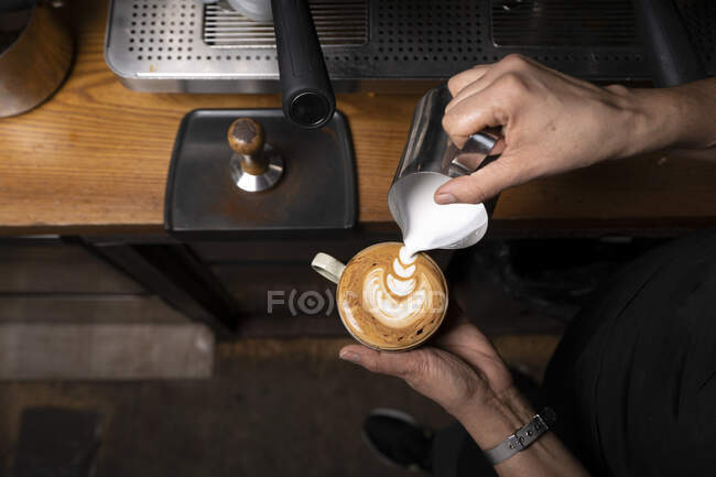 De acima mencionadas mãos de colheita de empregado profissional preparando cappuccino com padrão no topo na cafeteria — Fotografia de Stock