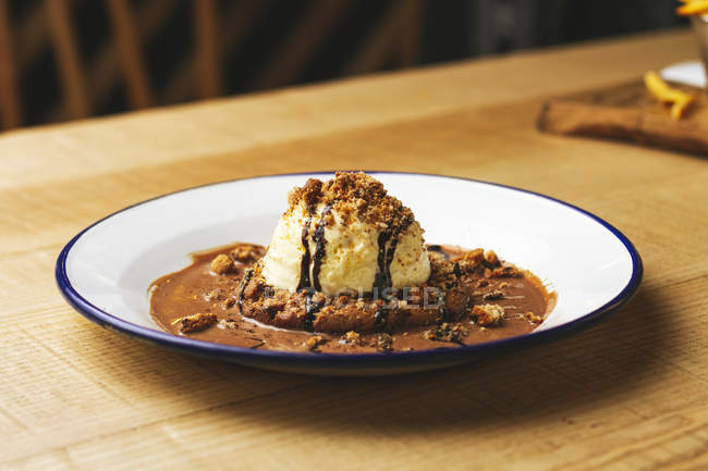 Hambúrguer doce saboroso com migalhas de chocolate e nozes servidas na placa na mesa de madeira — Fotografia de Stock