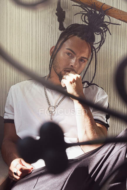 Handsome African American man with braided hair sitting on stairs and looking at camera indoors — Stock Photo