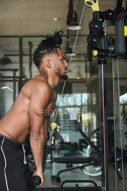 Black guy using exercise machine in gym, side view — Stock Photo
