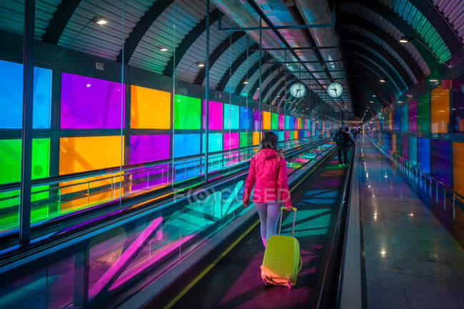 Unrecognizable woman with suitcase riding mowing walkway near colorful panels inside Madrid Barajas Airport in Spain — Stock Photo