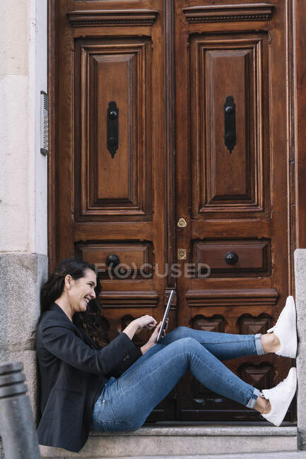 Side view of beautiful woman using digital tablet while relaxing on threshold of old wooden door — Stock Photo
