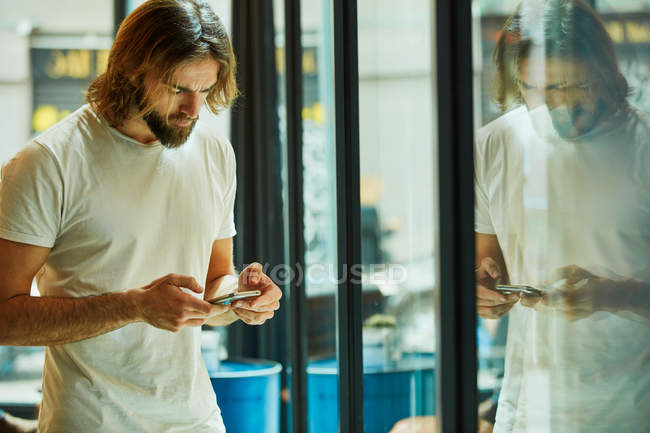 Giovane uomo bello barbuto che tiene il telefono cellulare e messaggistica appoggiata sulla superficie dello specchio — Foto stock