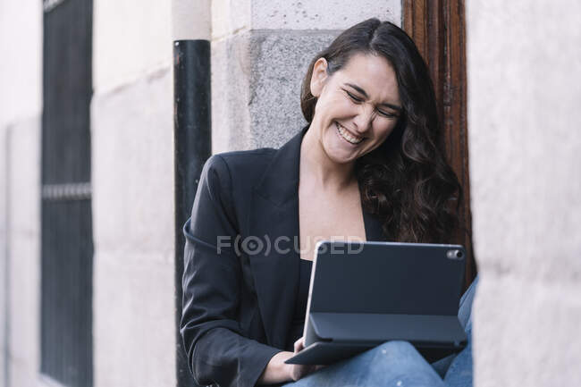 Mulher bonita usando tablet digital enquanto relaxa no limiar de uma porta do edifício — Fotografia de Stock