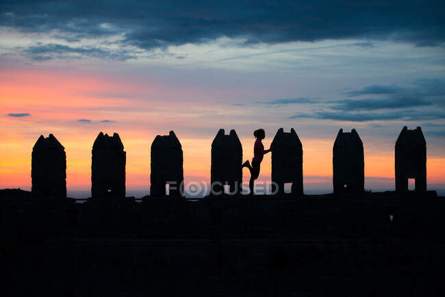 Silhouette of unrecognizable woman standing leaning on rectangular stone sculptures in gloomy breathtaking sunset sky — Stock Photo