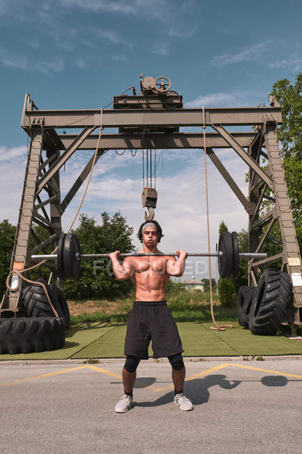 Young guy with barbell in outdoor gym — Stock Photo