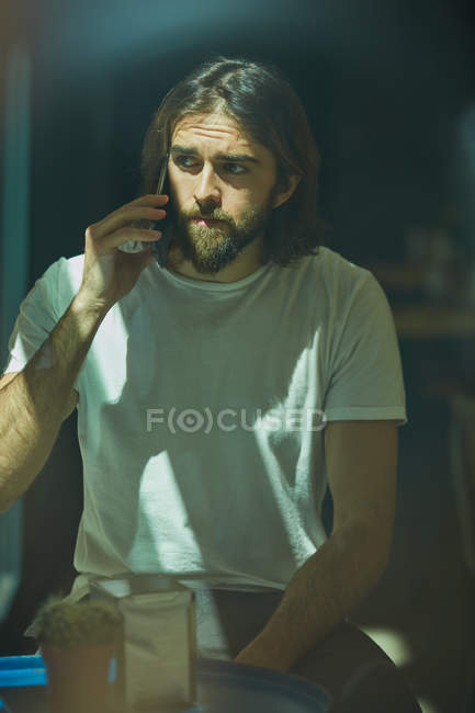 Young bearded handsome man in cafe behind window talking on phone — Stock Photo