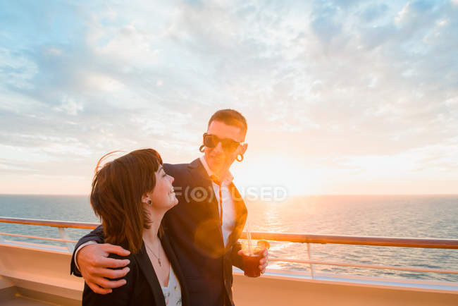 Young attractive couple drinking red beverage with straws from one glass on background of sunset sea — Stock Photo