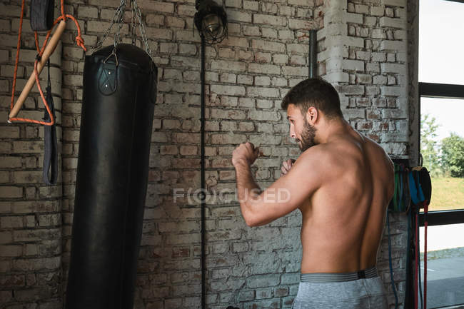 Young strong athlete boxing with bag in gym — Fotografia de Stock