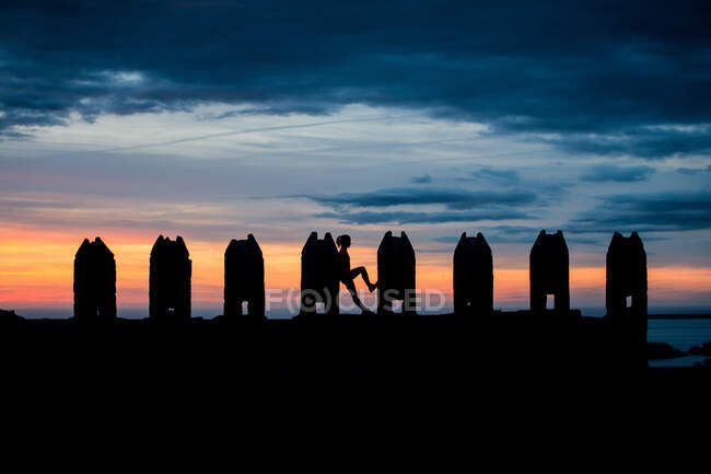 Silueta de mujer irreconocible de pie apoyada en esculturas rectangulares de piedra en el cielo sombrío impresionante puesta de sol - foto de stock