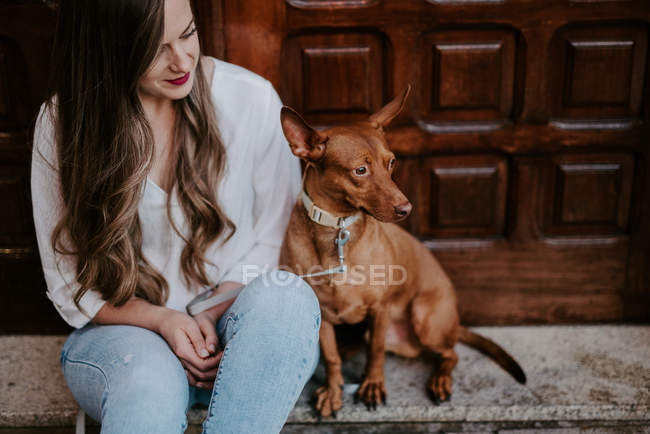 Casual woman with hound dog sitting on concrete step on street — Stock Photo