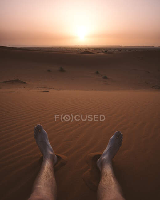 Crop male barefoot legs on sand of endless desert dune in hazy light of sunset, Morocco — Stock Photo