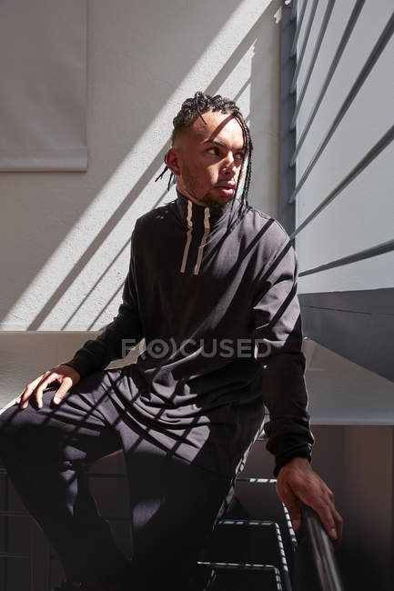 Молодой афроамериканец сидит на металлических перилах и смотрит в сторону — стоковое фото