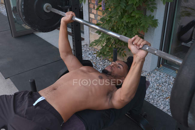 Desde arriba, un hombre afroamericano sin escrúpulos ejerce con la campana mientras entrena en gimnasio al aire libre. - foto de stock