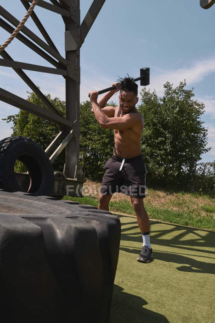 Musclé noir gars marteler pneu dans la salle de gym extérieure — Photo de stock