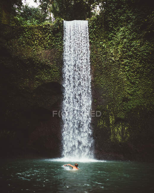 Vista lateral do homem nadando em águas claras do lago com cachoeira no fundo, Bali — Fotografia de Stock