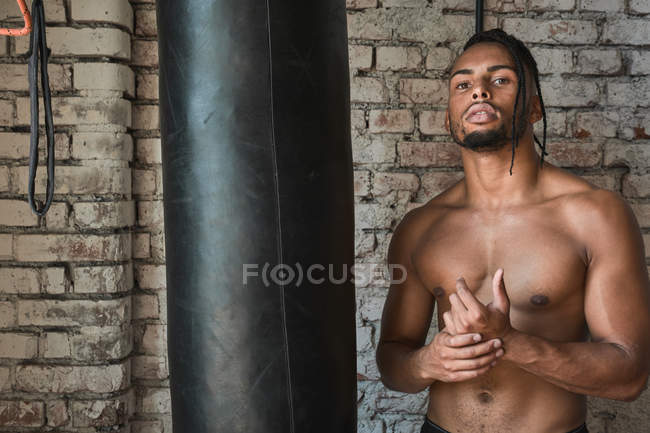 Confident black boxer in gym posing with boxing bag — Stock Photo