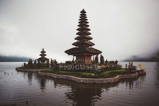 Небольшой комплекс молитвенной пагоды с зеленым садом вокруг построен в воде на берегу против тумана, Бали — стоковое фото