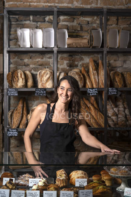 Красивая женщина в черном фартуке продает французский багет в пекарне — стоковое фото
