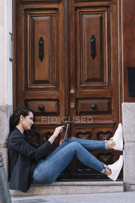 Vista lateral da mulher bonita usando tablet digital enquanto relaxa no limiar da velha porta de madeira — Fotografia de Stock