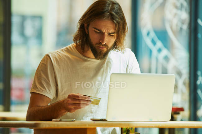 Junger bärtiger schöner Mann sitzt draußen im Café und arbeitet mit Laptop auf dem Tisch — Stockfoto