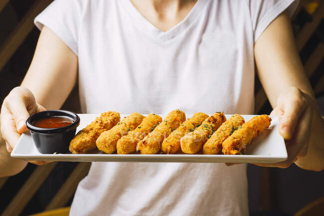 Аппетитные жареные хрустящие куриные палочки и ароматический красный соус на белой тарелке в руках — стоковое фото