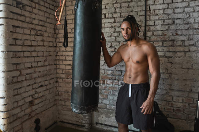 Впевнений чорний боксер в тренажерному залі позує з боксерською сумкою — стокове фото