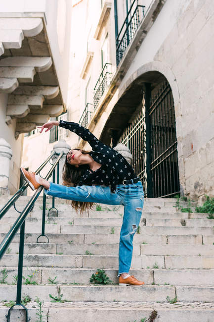 Молода струнка випадкова жінка розтягується і танцює на сходах під час витончених танців на вулиці старого міста — стокове фото