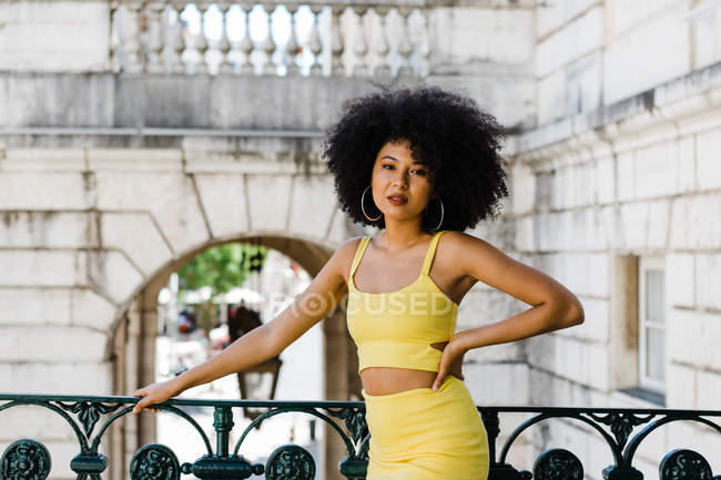 Afrikanisch-amerikanische Frau in gelbem Anzug und Jeansjacke steht und blickt in die Kamera auf urbanem Hintergrund — Stockfoto