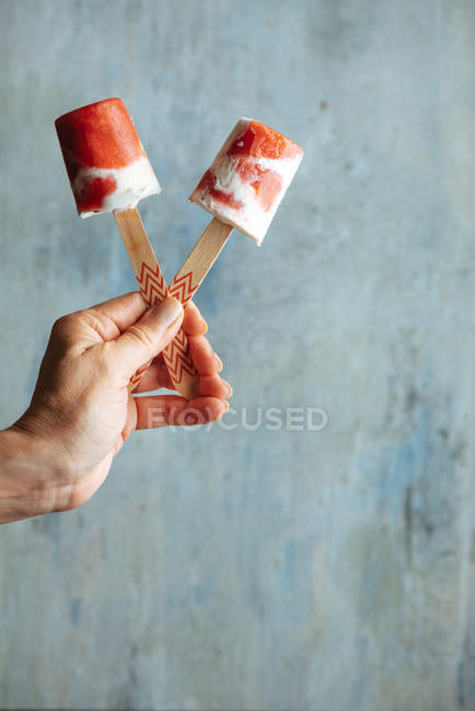 Female hand holding watermelon and cream ice-cream against light blue background — Stock Photo