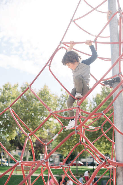 Kleiner Junge hängt am Seil, während er im hellen Licht auf Spielplatz Kletternetz läuft — Stockfoto