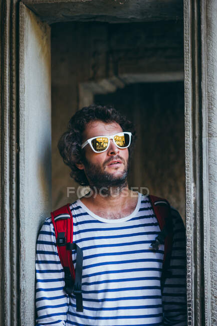 Adult bearded man in sunglasses and with backpack standing in stone door frame, Thailand — Stock Photo