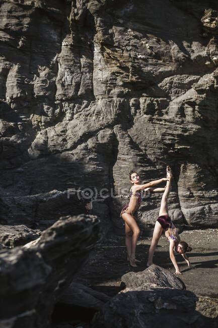 Female gymnasts with raised legs on seashore — Stock Photo