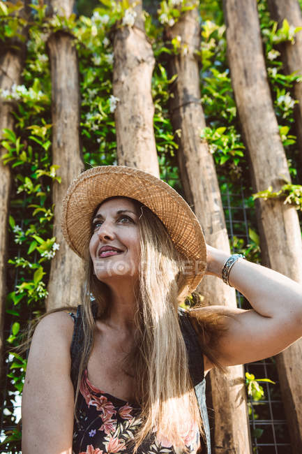 Content adult woman in summer straw hat smiling on street against green trees — Stock Photo