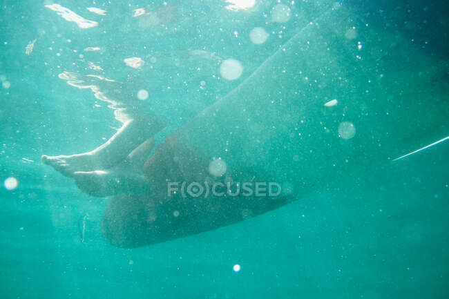 From below of crop legs underwater hanging from floating boat in sunbeams, Thailand — Stock Photo