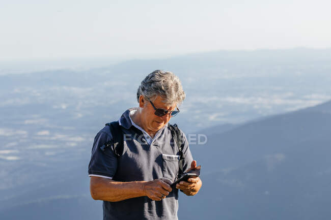 Homem sênior usando seu telefone celular na montanha — Fotografia de Stock