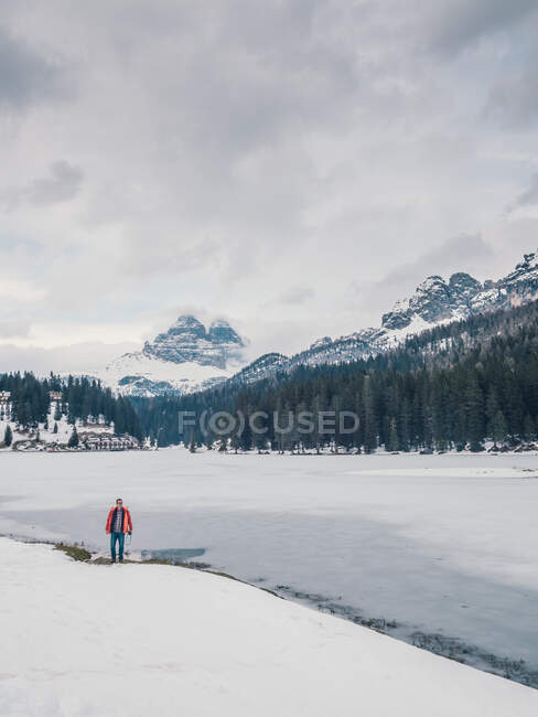 Яркая фигура человека в теплой одежде, стоящего в снежной зоне на фоне скалистых гор и густого леса — стоковое фото