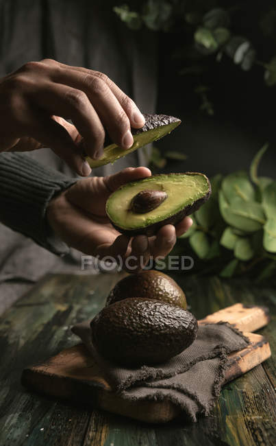 Menschenhände halten halbierte Avocado über Holztisch — Stockfoto