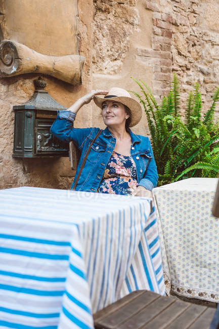 Woman in straw hat and dress sitting on terrace of restaurant in medieval town — Stock Photo