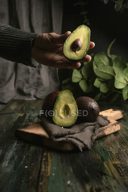 Mão humana segurando abacate pela metade sobre mesa de madeira — Fotografia de Stock