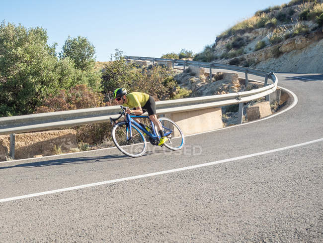 Healthy man riding bicycle on mountain road in sunny day — Stock Photo