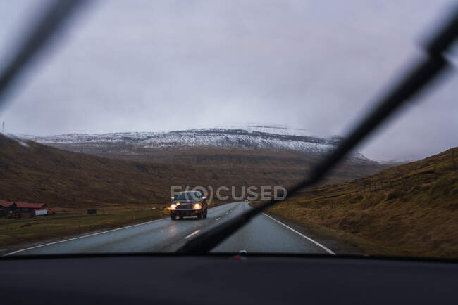 De dentro de uma vista de carro de uma estrada em um dia chuvoso com um fundo de montanha nevado — Fotografia de Stock