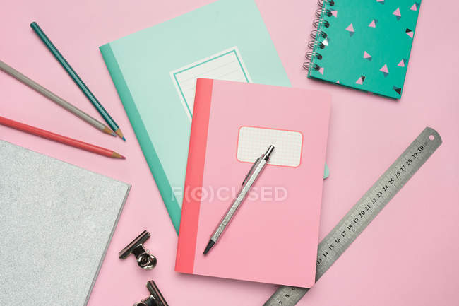 Composizione di quaderni colorati, penna, matite, righello e graffette disposti su scrivania rosa — Foto stock
