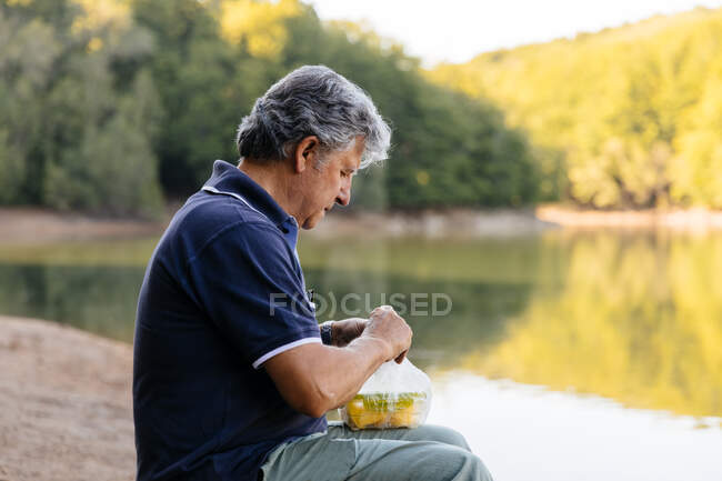 Vista lateral del hombre preparándose para comer fruta en el bosque - foto de stock