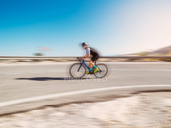 Blurred motion of healthy man riding a bicycle on road in sunny day — Stock Photo