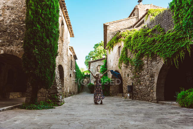 Visão traseira da mulher irreconhecível de vestido e chapéu estendendo os braços, na rua de uma cidade medieval — Fotografia de Stock
