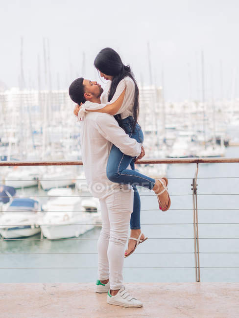 Vista lateral do lindo jovem casal em roupas leves de ligação e abraço com amor e ternura na doca no porto — Fotografia de Stock