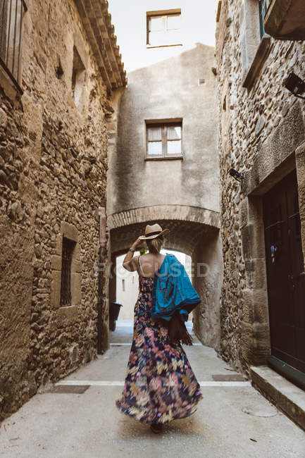 Vista trasera de una mujer irreconocible con vestido y sombrero caminando por la calle de una ciudad medieval - foto de stock