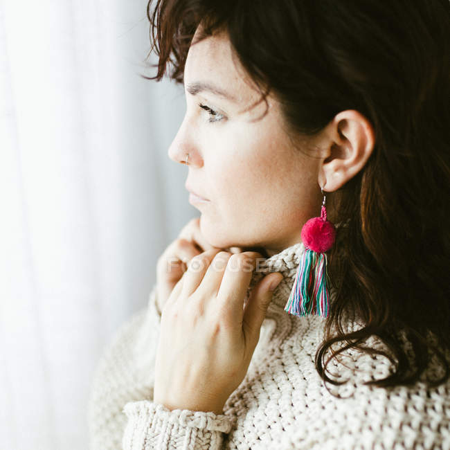 Side view of attractive dreamy young brunette with bright handmade earring of colorful threads — Stock Photo